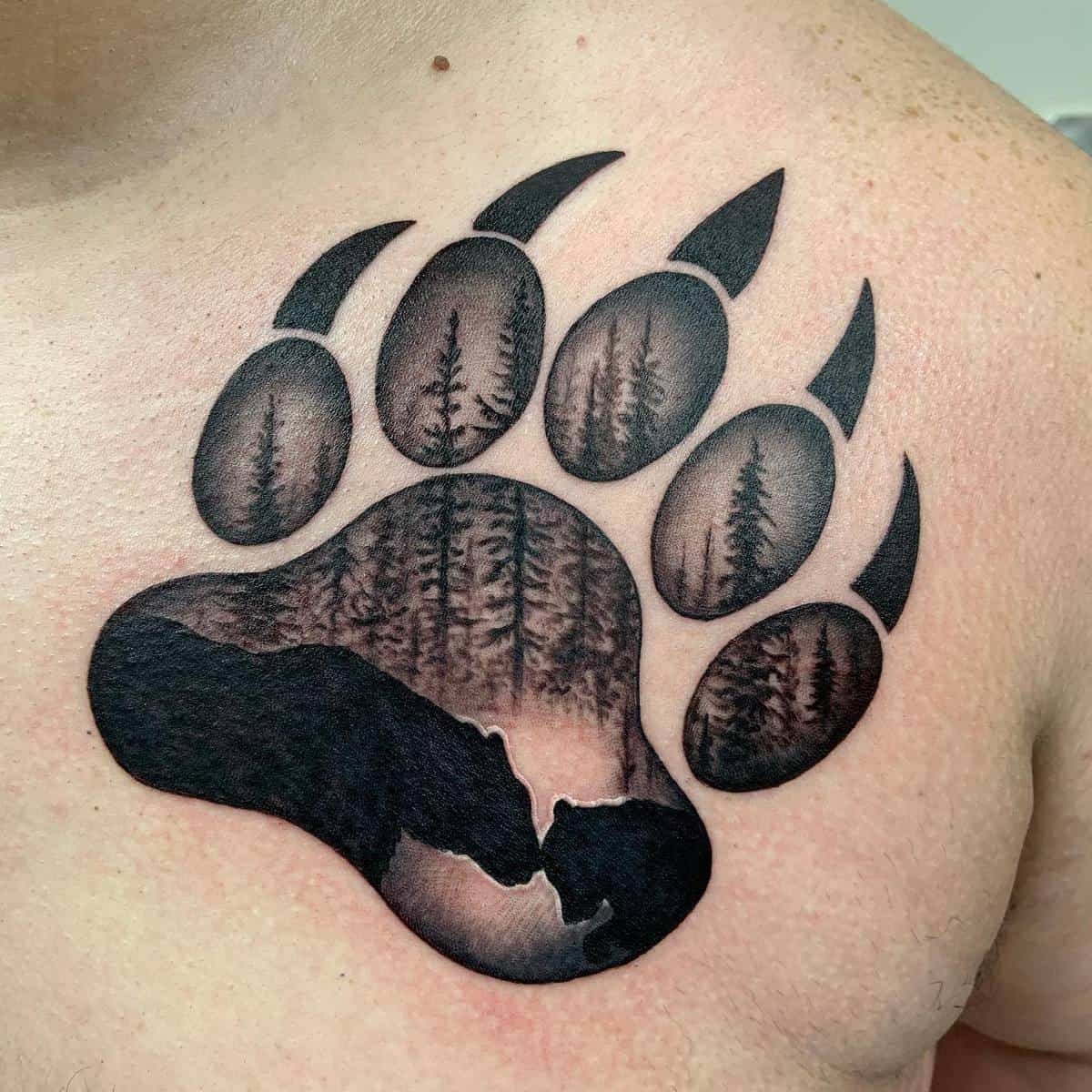 Tattoo of a bear paw with trees and a bear silhouette inside on chest