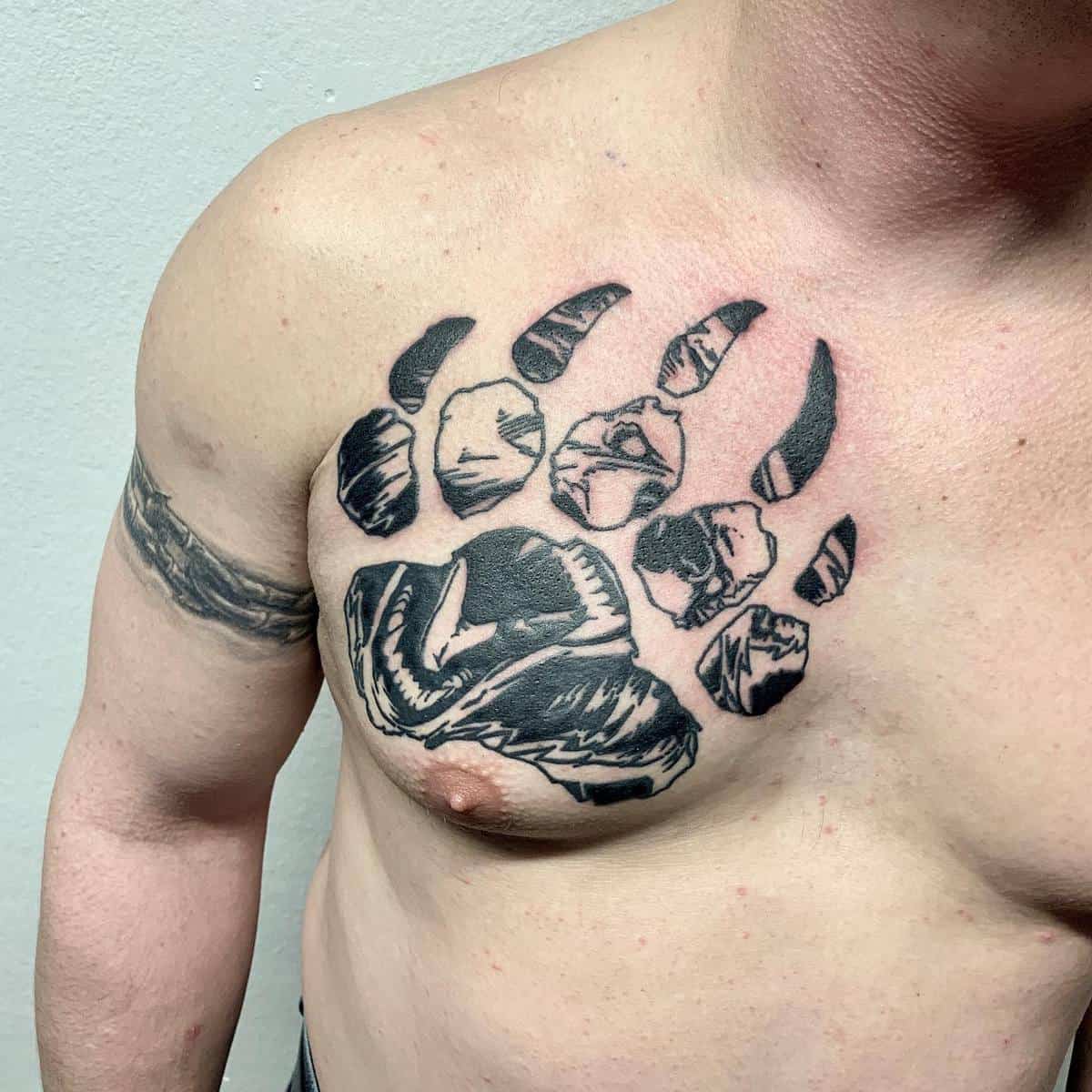 Chest tattoo of a bear paw print with a face inside it covering the upper left chest area