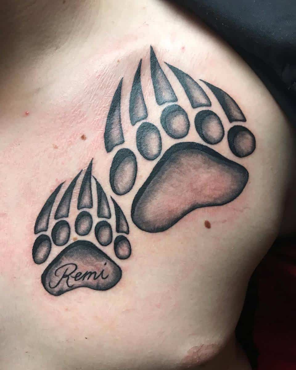 Bear paw tattoo with two bear paw prints, one with the name "Remi" inscribed in the pad
