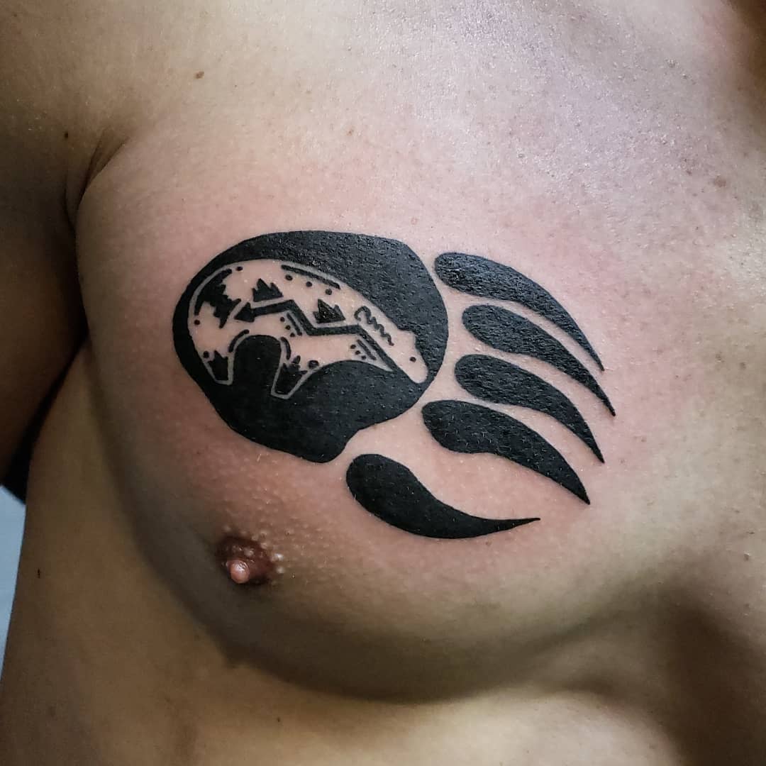 Bear paw tattoo featuring a detailed landscape scene, including mountains, trees, and a river on a person's chest