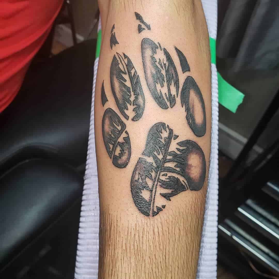Tattoo of a wolf paw print with feathers resembling a bear paw on a person's forearm