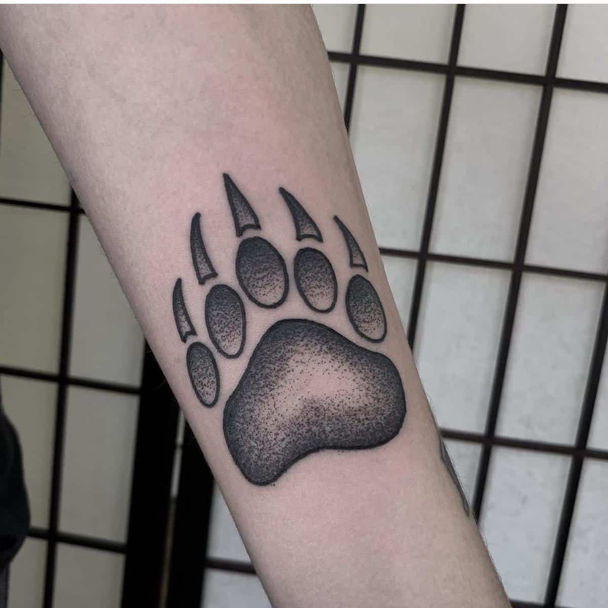 Tattoo of a bear paw on an arm with intricate shading and detailed claws