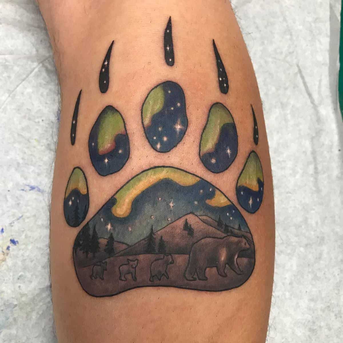 Bear paw tattoo with nature scene inside featuring bears, mountains, and starry night sky