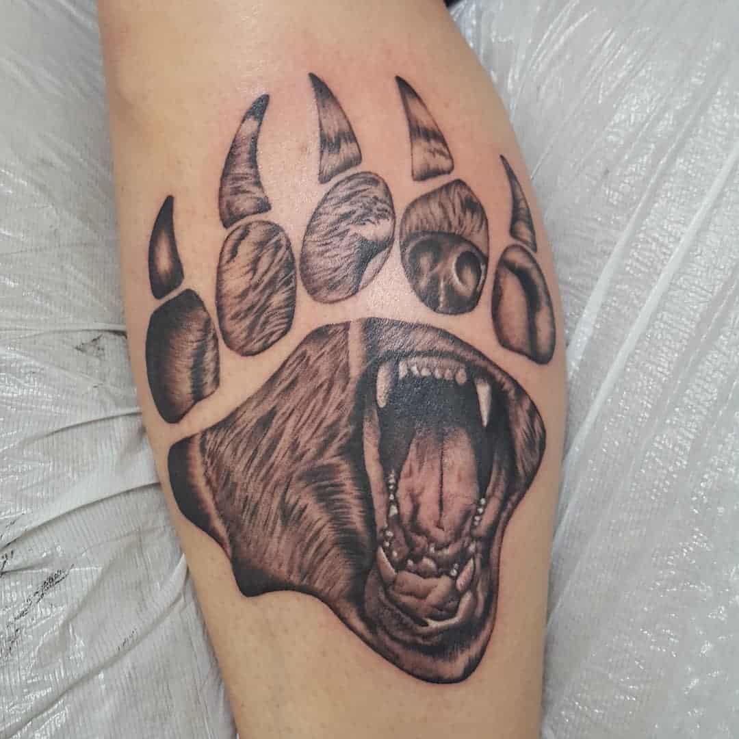 Tattoo of a bear's open mouth inside an outlined bear paw on a person's arm