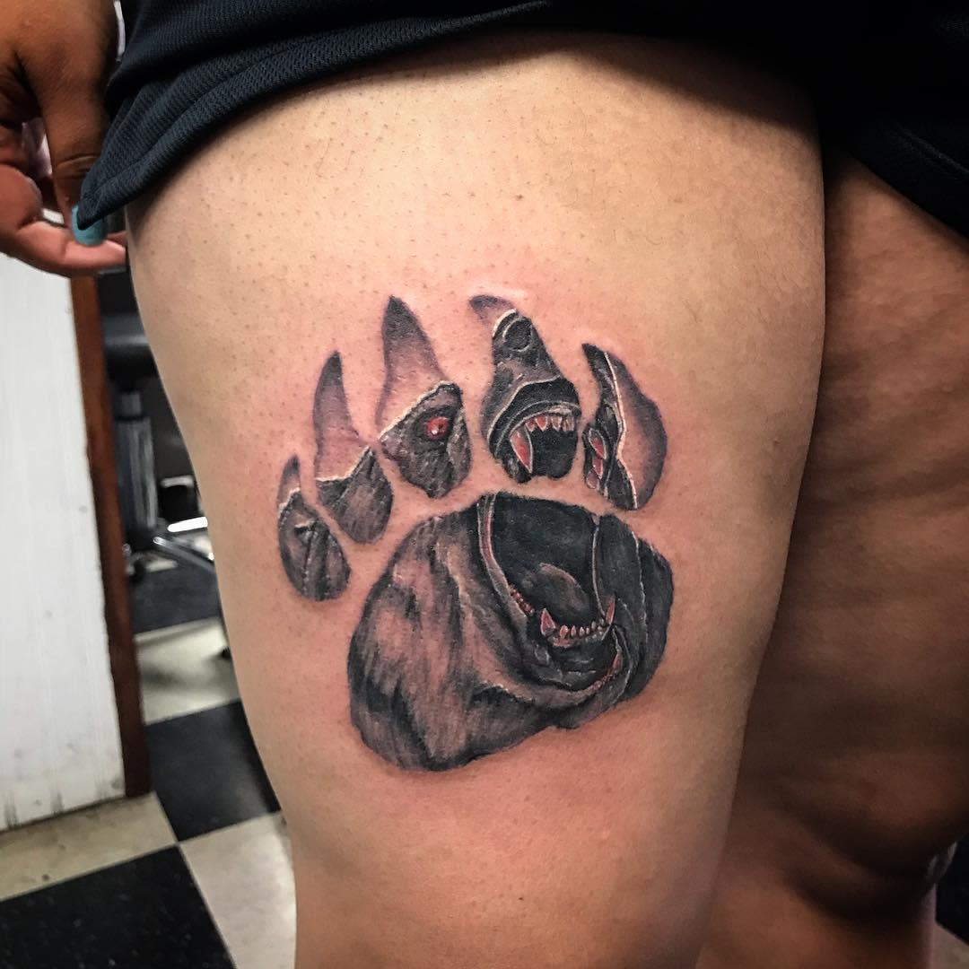 Tattoo of a bear's paw print with a growling bear face inside on thigh