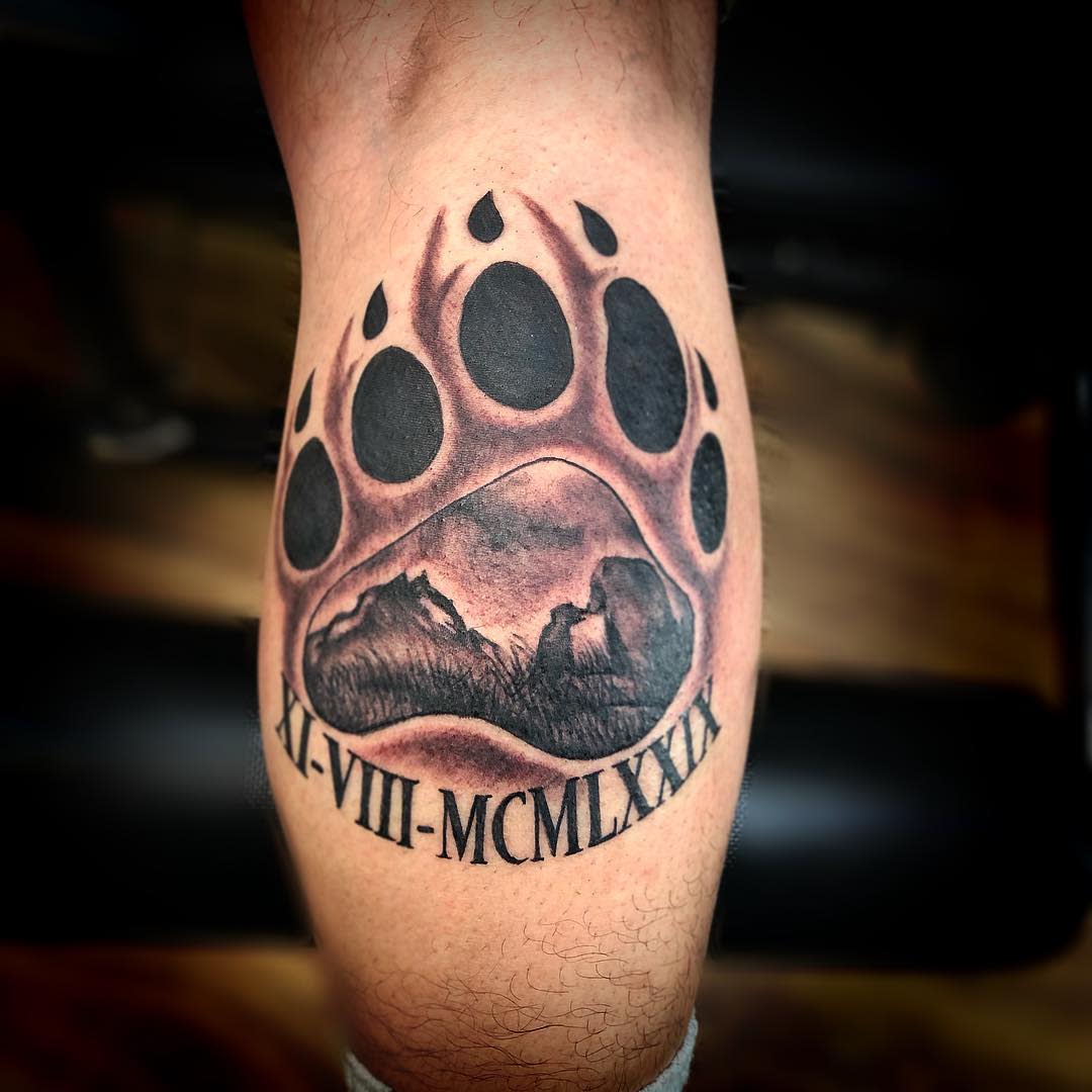 Tattoo of a detailed bear paw featuring a mountain scene and Roman numerals XI-VIII-MCMLXXIX