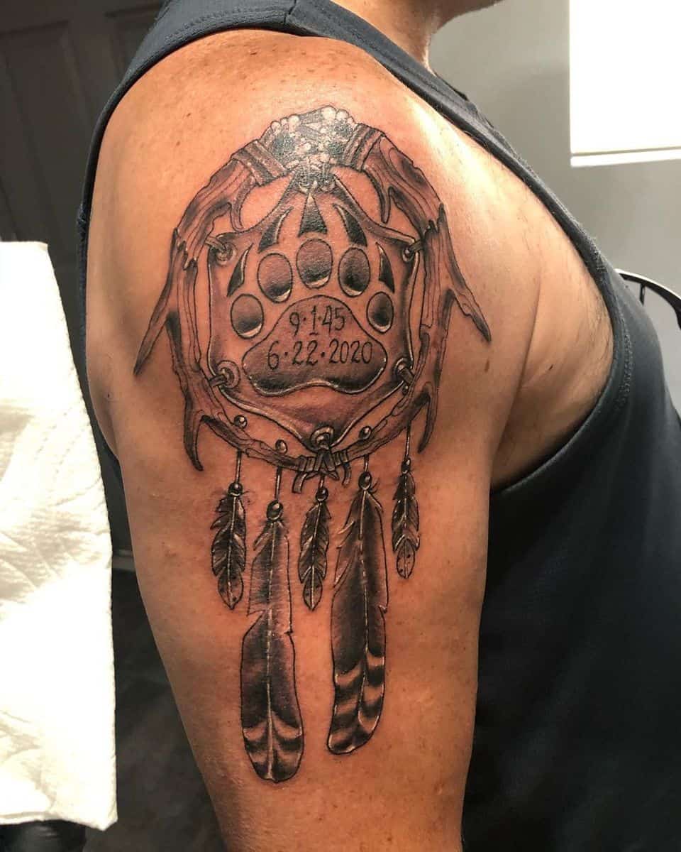 A dreamcatcher with a bear paw and important dates tattooed on an upper arm