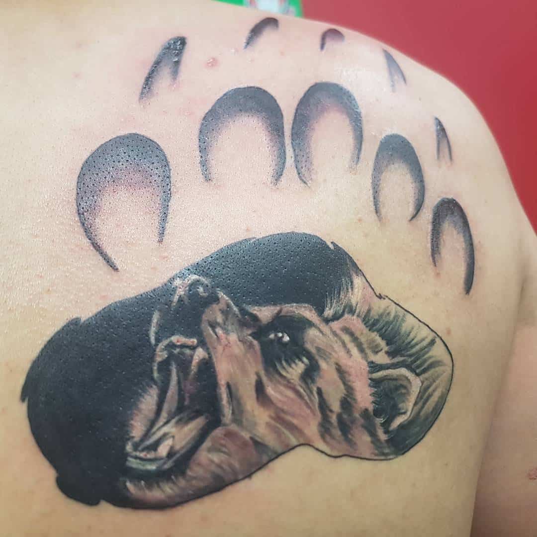 Tattoo on shoulder: a realistic bear head below stylized bear paw prints, capturing rugged wilderness and primal strength
