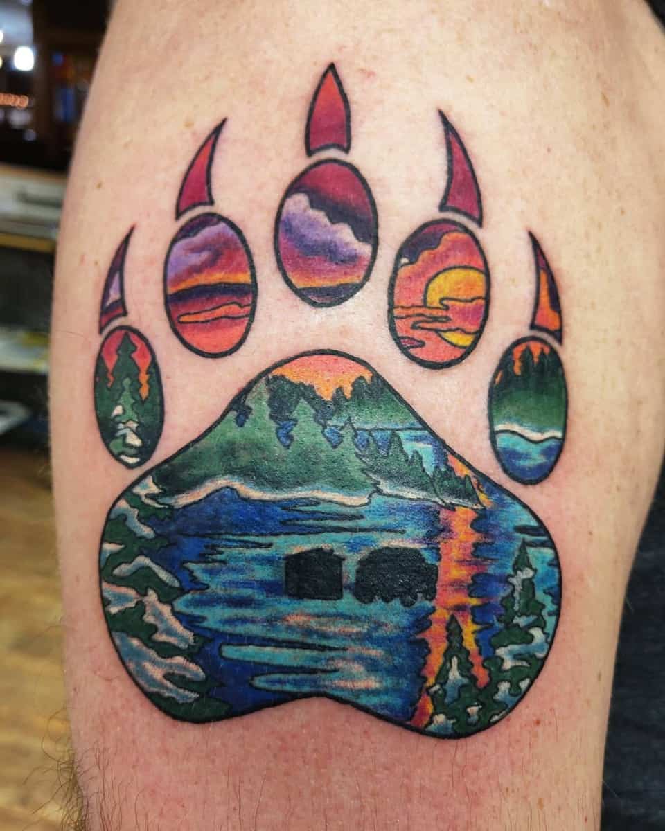 Tattoo of a bear paw with colorful nature scenery intricately detailed inside each pad on a person's skin