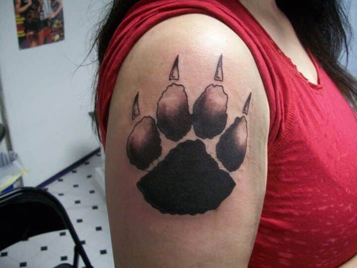 A woman with a large, realistic bear paw tattoo on her upper arm, wearing a vibrant red shirt