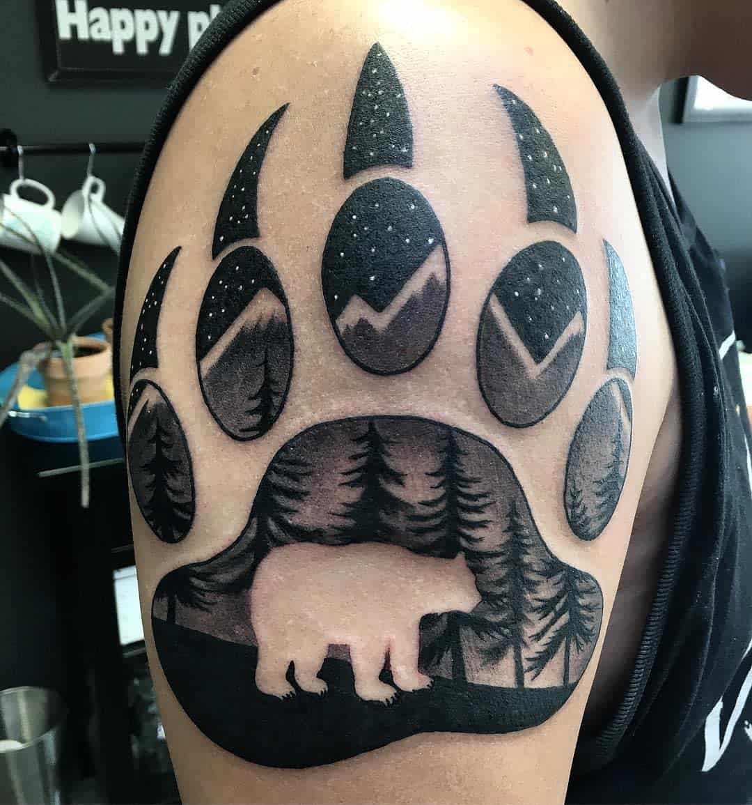 Tattoo of a bear paw with nature scene, features a bear, trees, and mountains