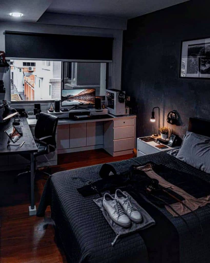 Modern bedroom with a desk setup, computer, and black bedding, featuring a window that offers a city view