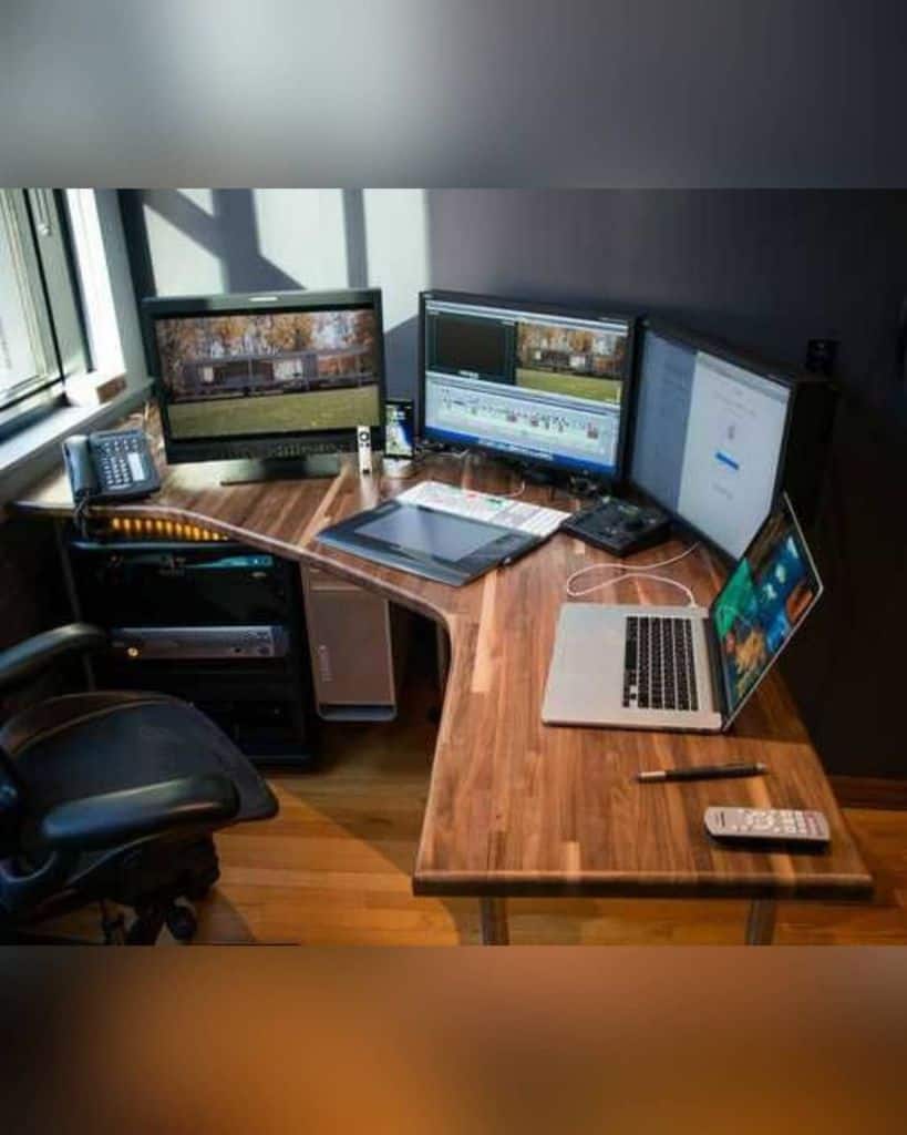 A corner desk setup with multiple monitors, a laptop, and a graphic tablet in a well-lit office space