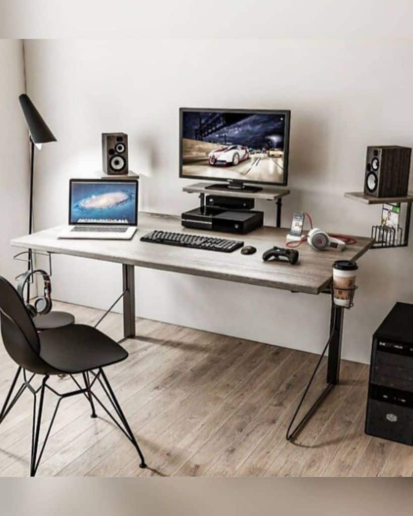 Minimalist workspace with a monitor, laptop, speakers, headphones, gaming controller, and coffee cup on a wooden desk