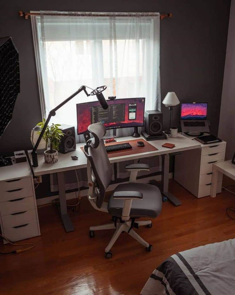 A modern home office setup with dual monitors, a microphone, speaker, and a potted plant on a spacious desk