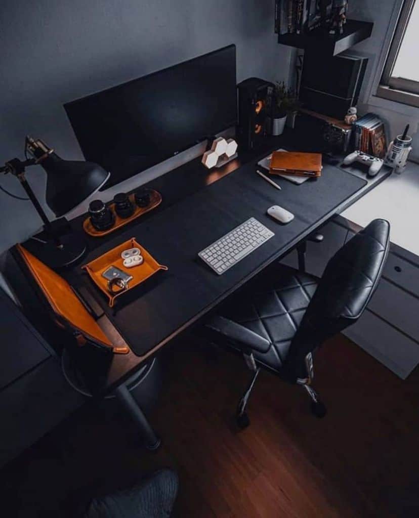A tidy workspace with a large monitor, keyboard, mouse, and leather accessories on a dark desk, beside a window