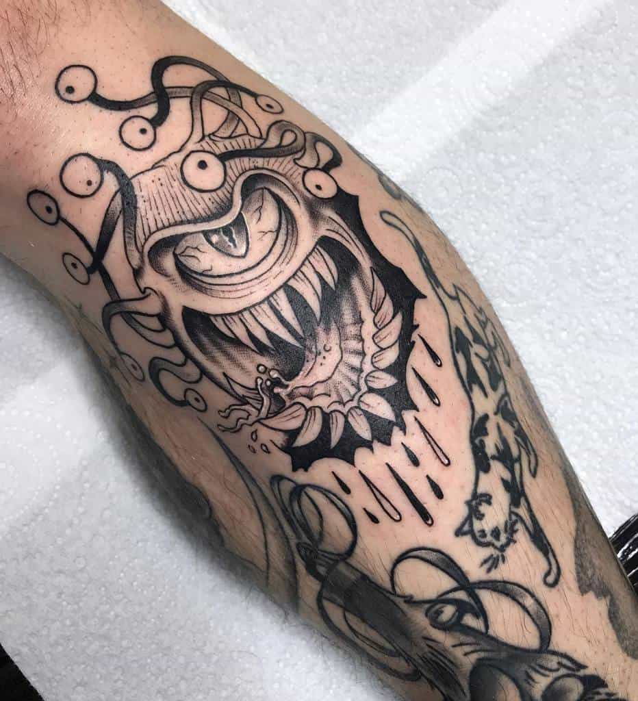 Detailed black and grey tattoo of a Dungeons & Dragons Beholder with sharp teeth, ominous eyes, and intricate shading