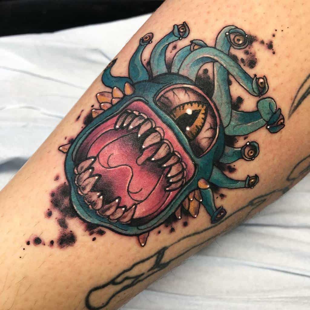 Colorful tattoo of a Beholder with a vivid teal body, sharp teeth, and striking eye details, framed by artistic splatter shading
