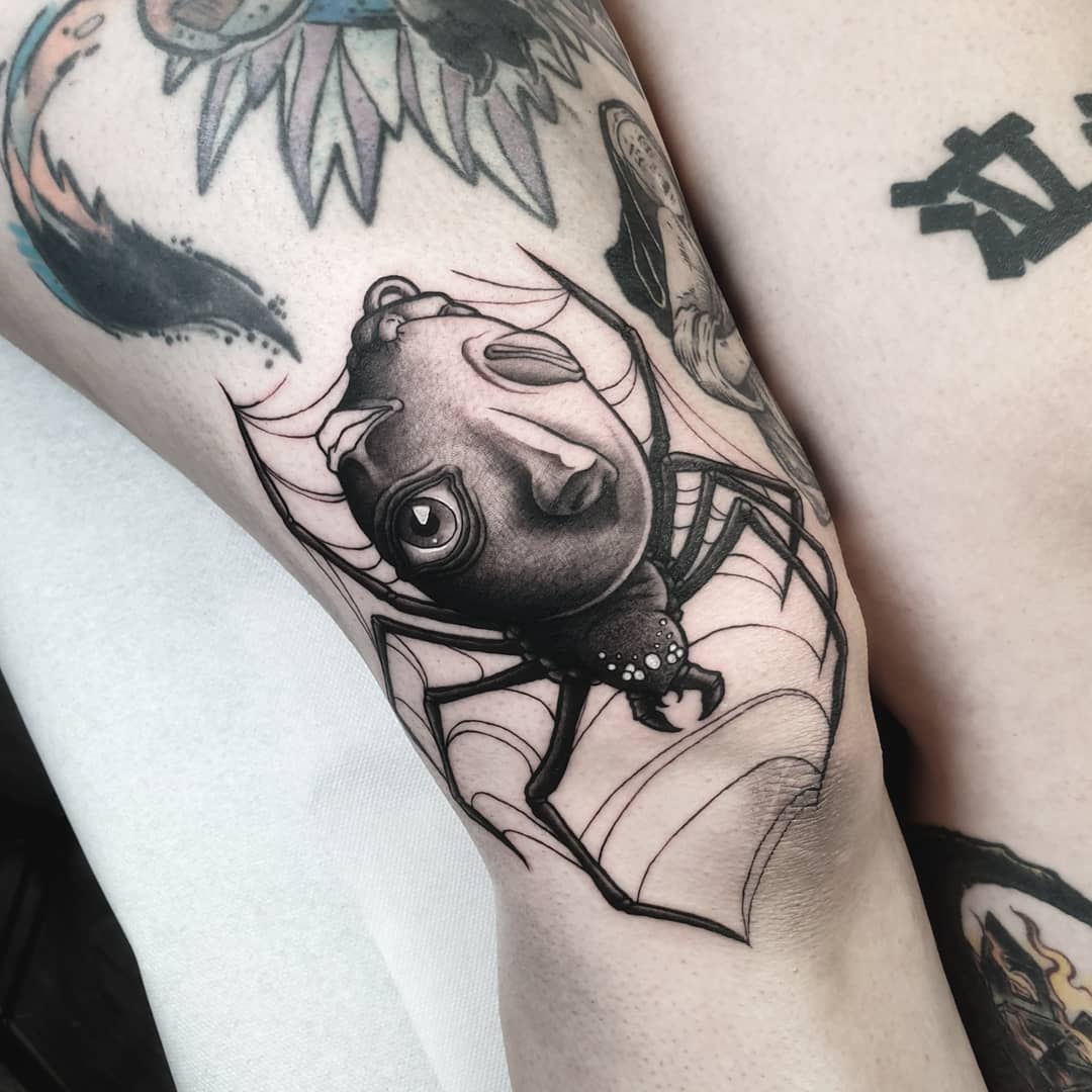 Black and white tattoo of a Behelit from Berserk, with spider legs and web, adding a dark twist