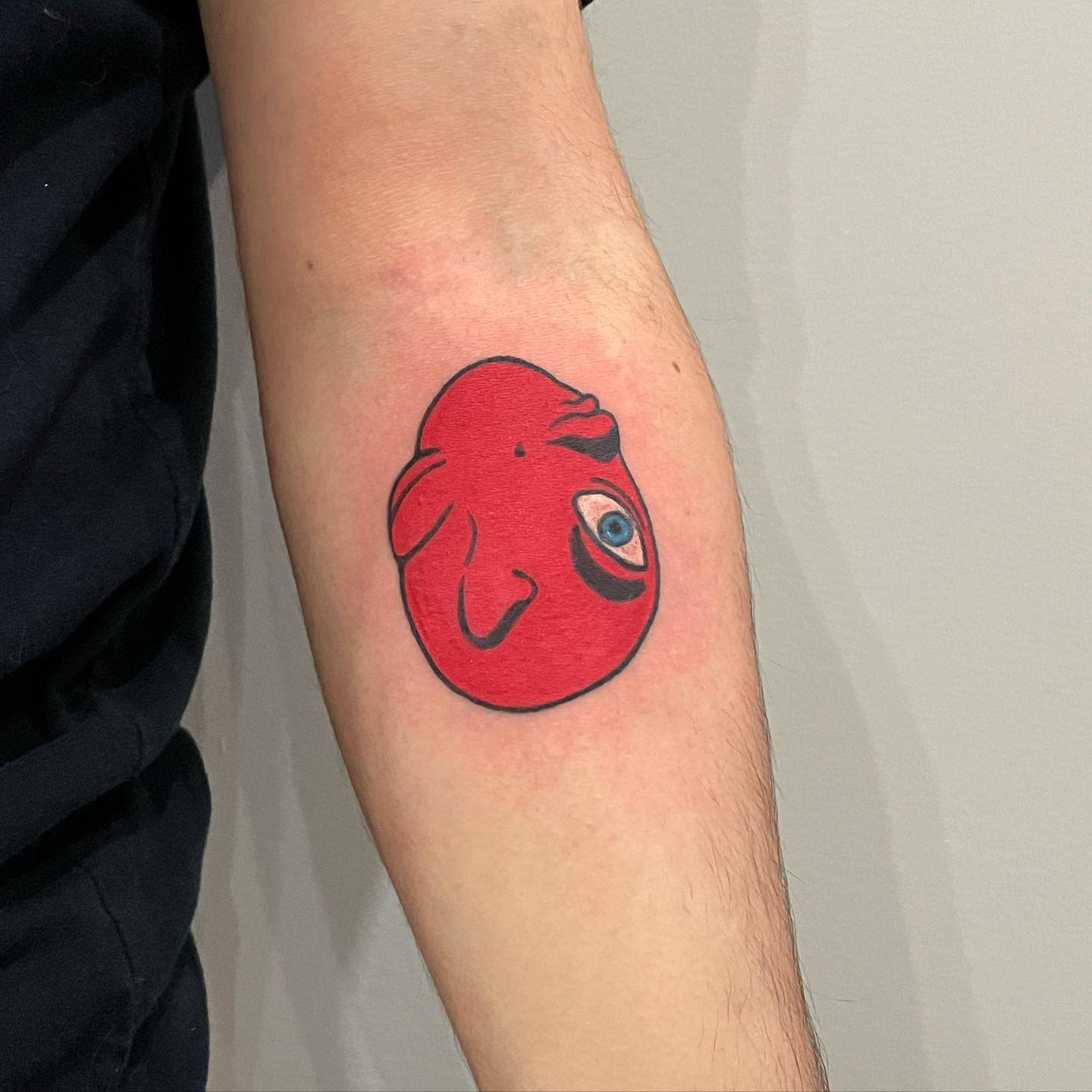 Tattoo of a red Behelit from Berserk, featuring its characteristic closed eyes and mouth