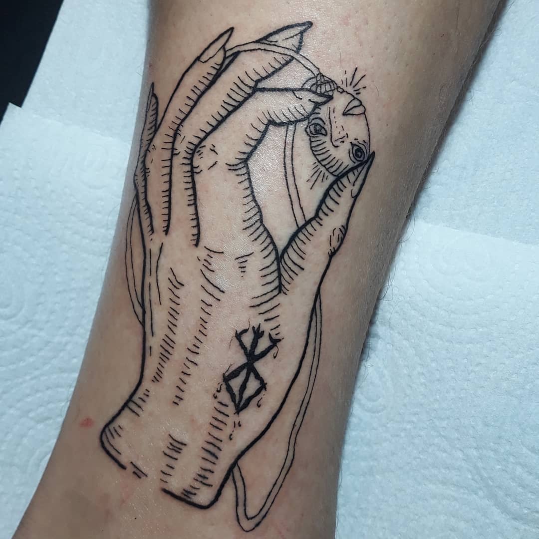 Line tattoo of a demonic hand holding a Behelit from Berserk, with a branded symbol on the wrist