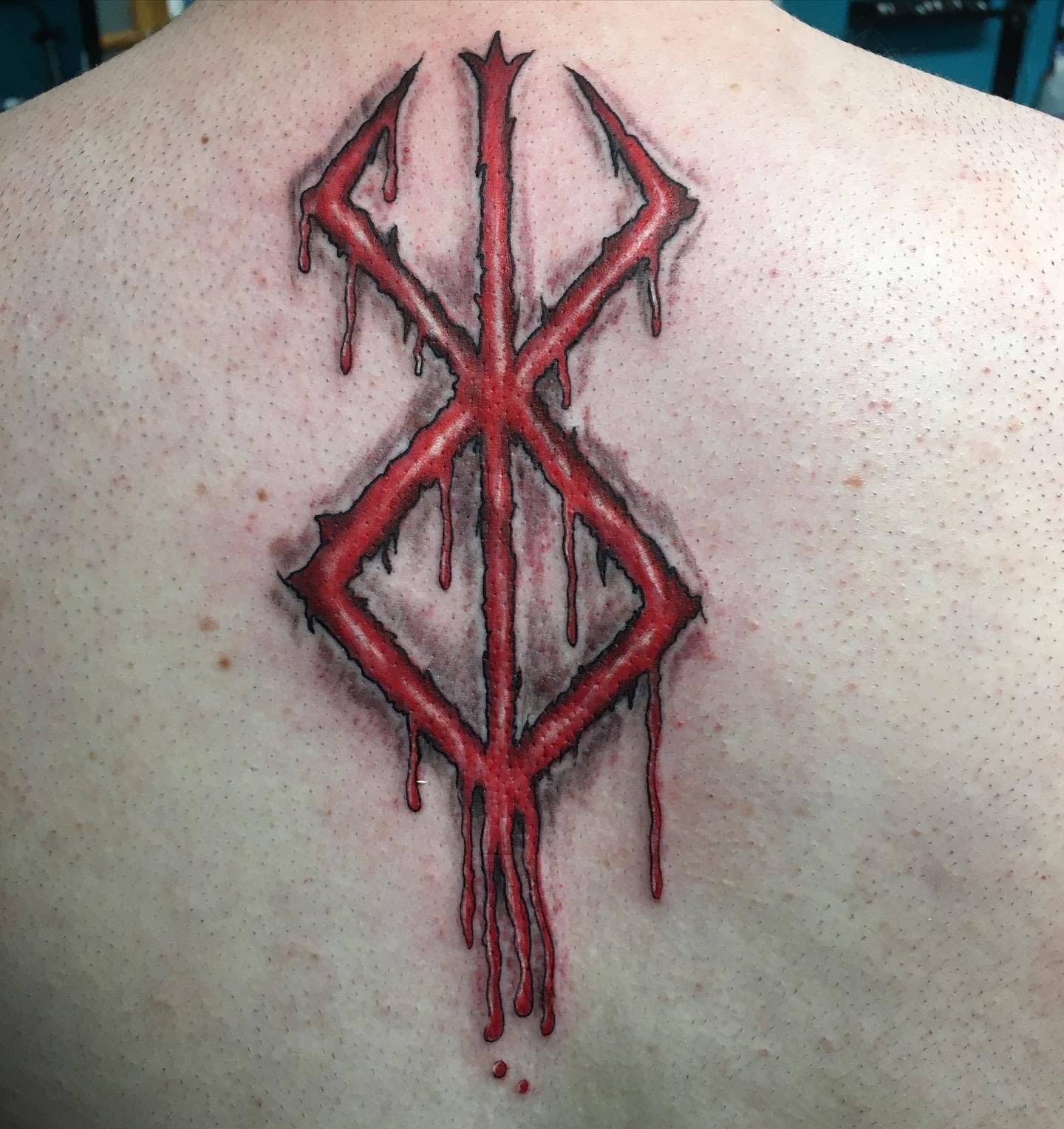 Tattoo of the Brand of Sacrifice from Berserk, depicted in red with a bleeding effect on the back