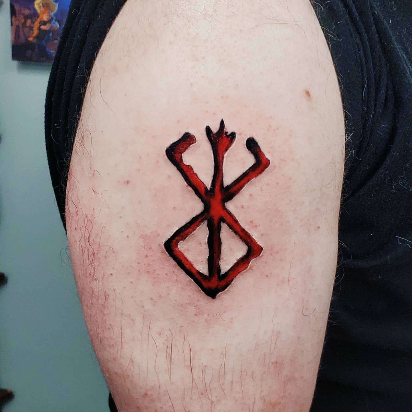 Tattoo of the Brand of Sacrifice from Berserk on the upper arm, depicted in red and black ink