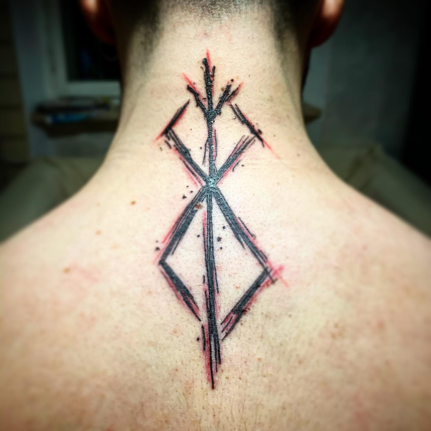 Abstract black and red geometric tattoo inspired by Berserk manga series, featuring sharp angles and intricate patterns on the back of the neck