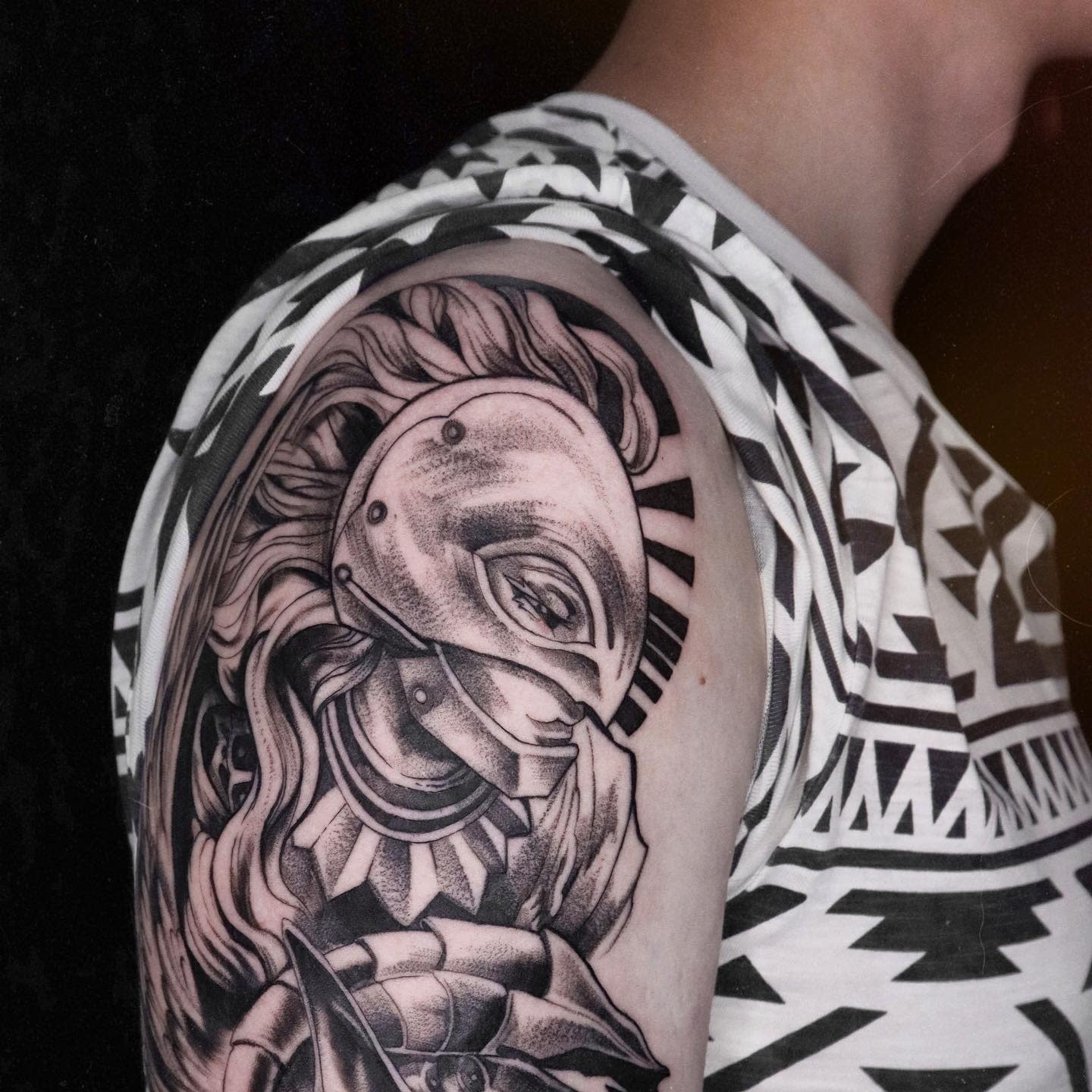 Detailed black and gray tattoo of Griffith from Berserk in his Hawk of Light armor on the upper arm, with intricate shading and flowing hair