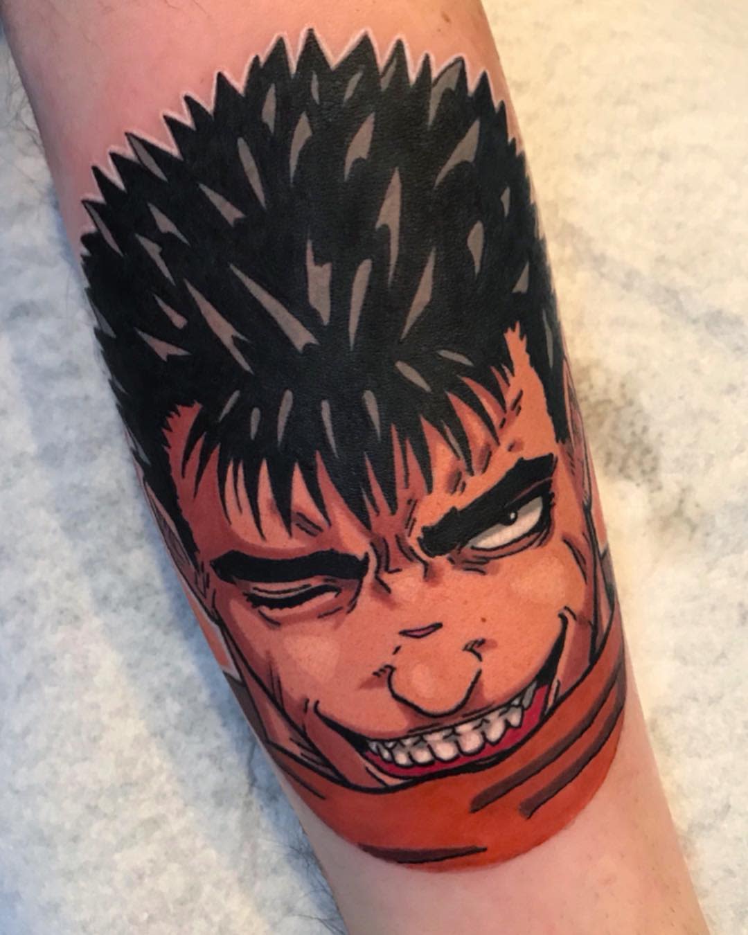 Bold, colorful tattoo of Guts from Berserk, capturing his iconic menacing grin and intense expression