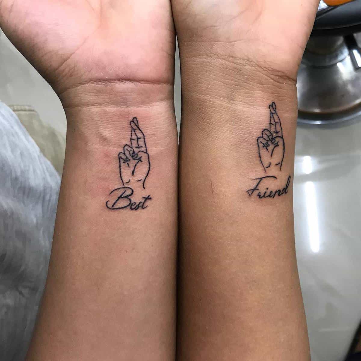 Two forearms with matching tattoos showing fingers crossed and the words "Best Friend"