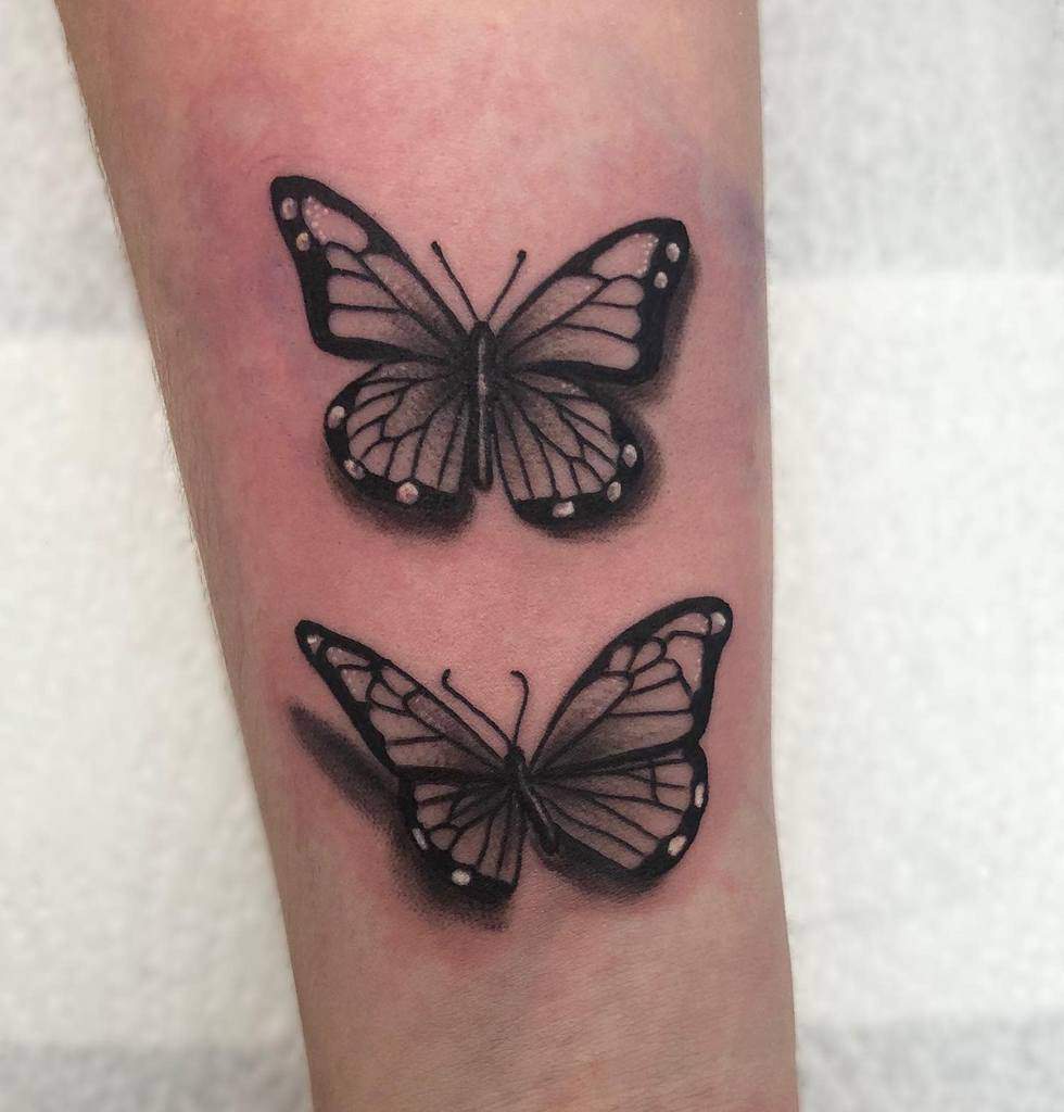 Tattoo of two black butterflies with intricate wing patterns on a forearm