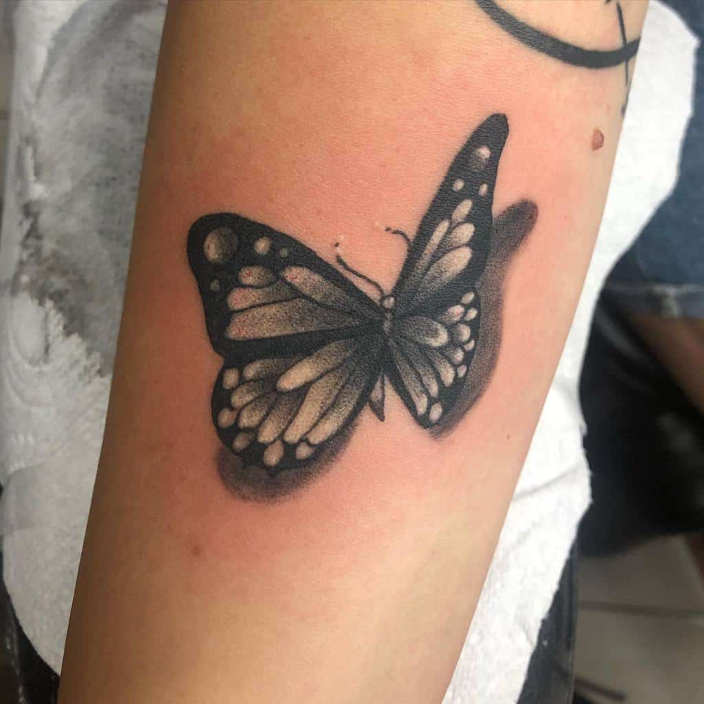 Tattoo of a shaded black and gray butterfly on an arm with detailed wings and white spots