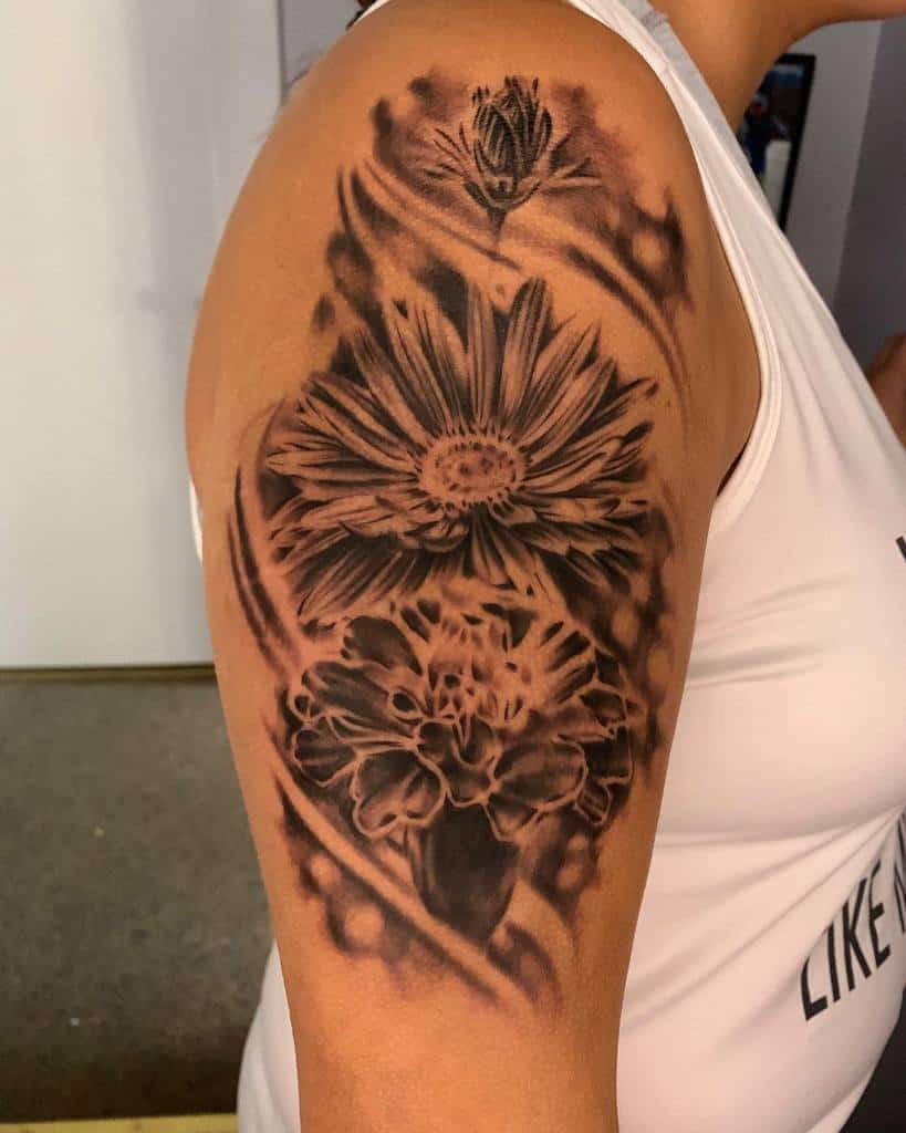 A detailed floral tattoo on a person's upper arm features multiple flowers including a striking aster