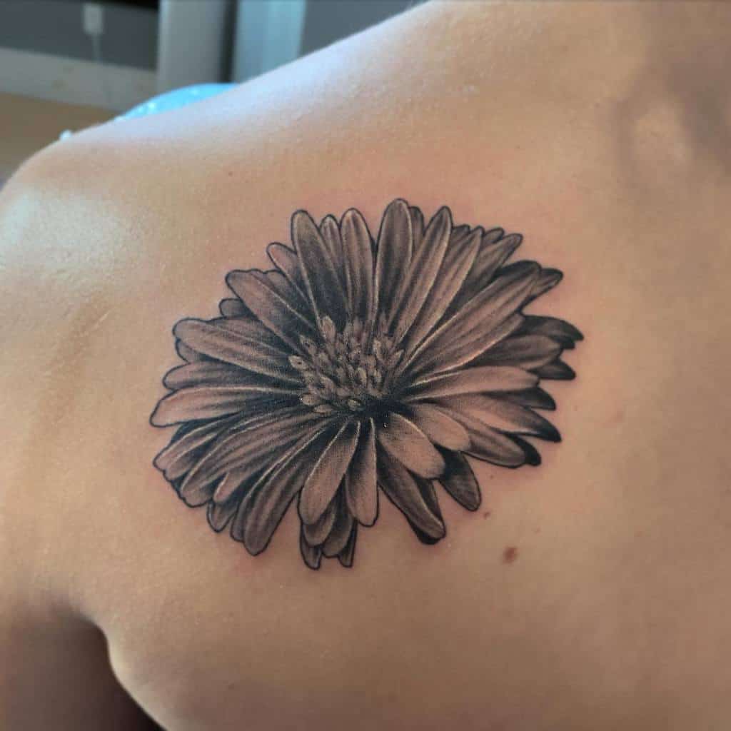 Black and white tattoo of a blooming aster flower on upper back