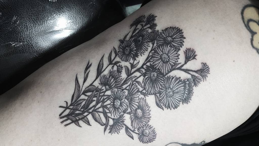 Black and grey tattoo of detailed aster flowers with leaves on a person's arm