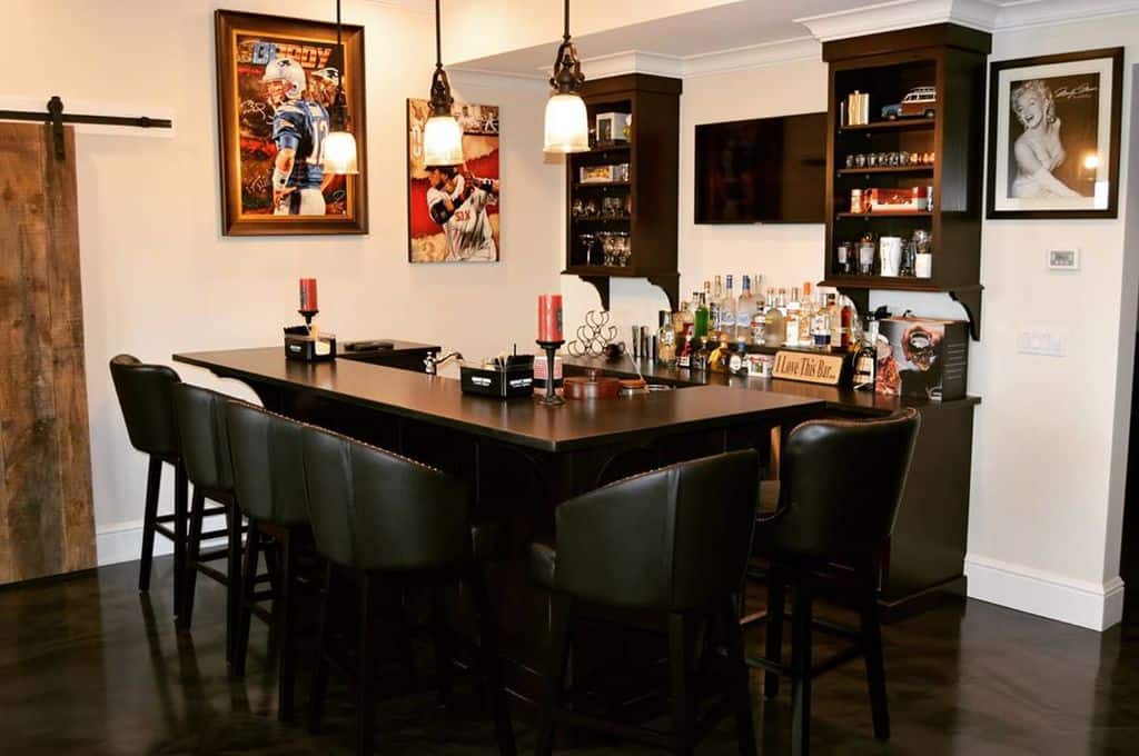 Stylish home bar with black leather stools, sports decor, and framed art in a cozy basement.
