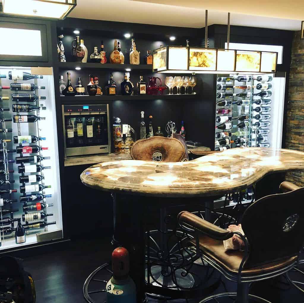 Luxury basement bar with wine cellar, leather stools, and illuminated marble countertop.