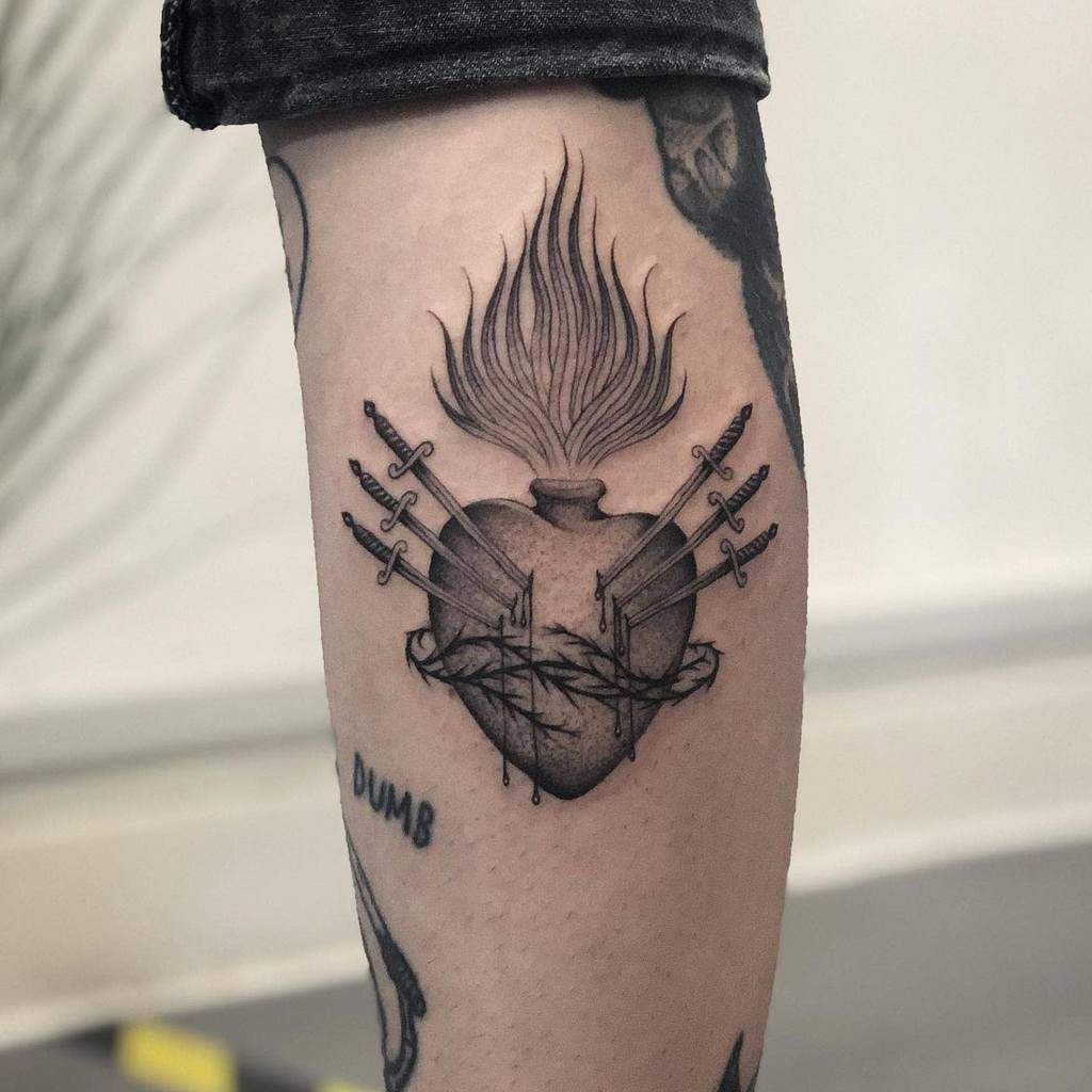 Black and grey Sacred Heart tattoo with flames, wrapped in thorns, and pierced by six swords, symbolizing pain and resilience