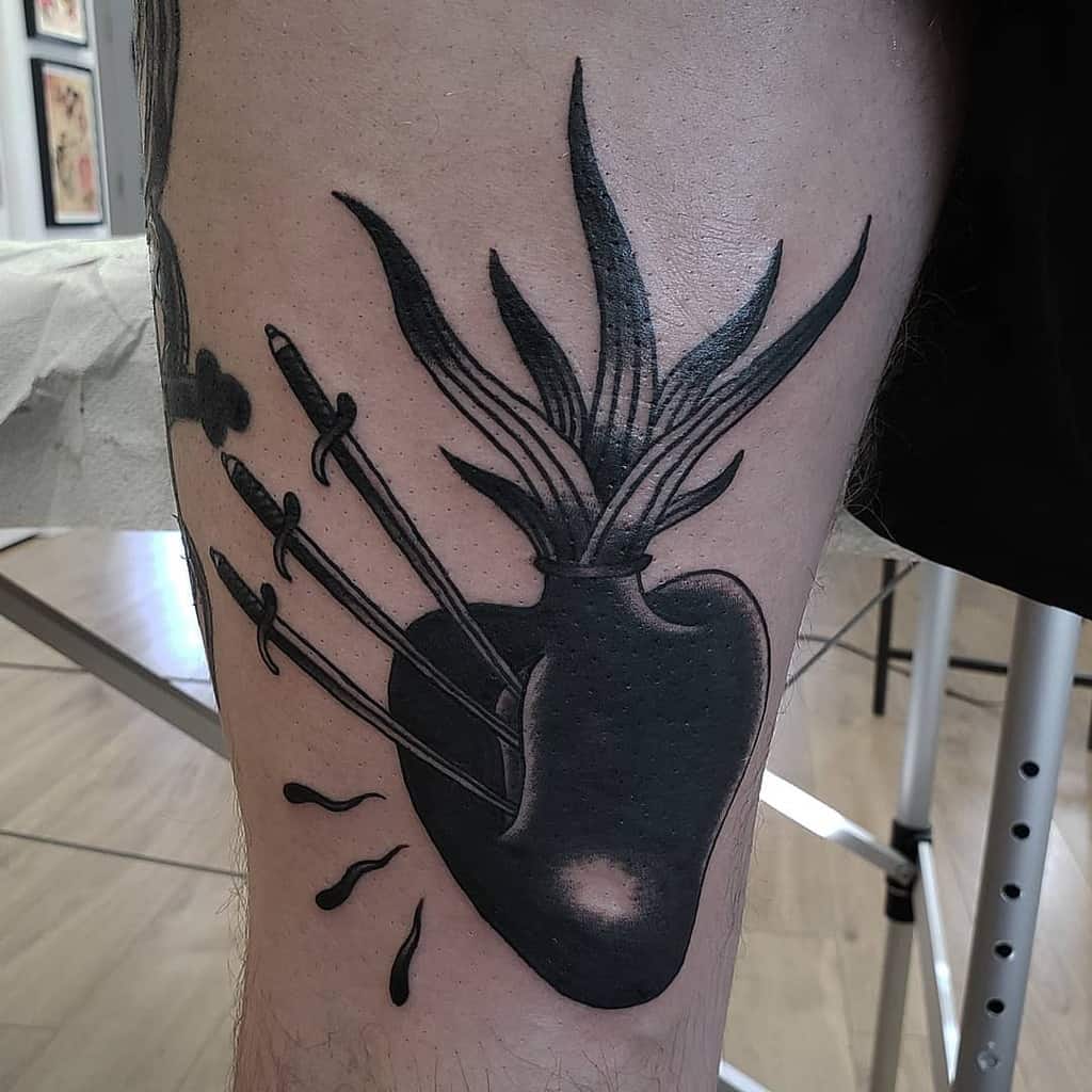 Tattoo of an anatomical heart with leaves and three swords piercing it, bleeding elegantly on a person's thigh