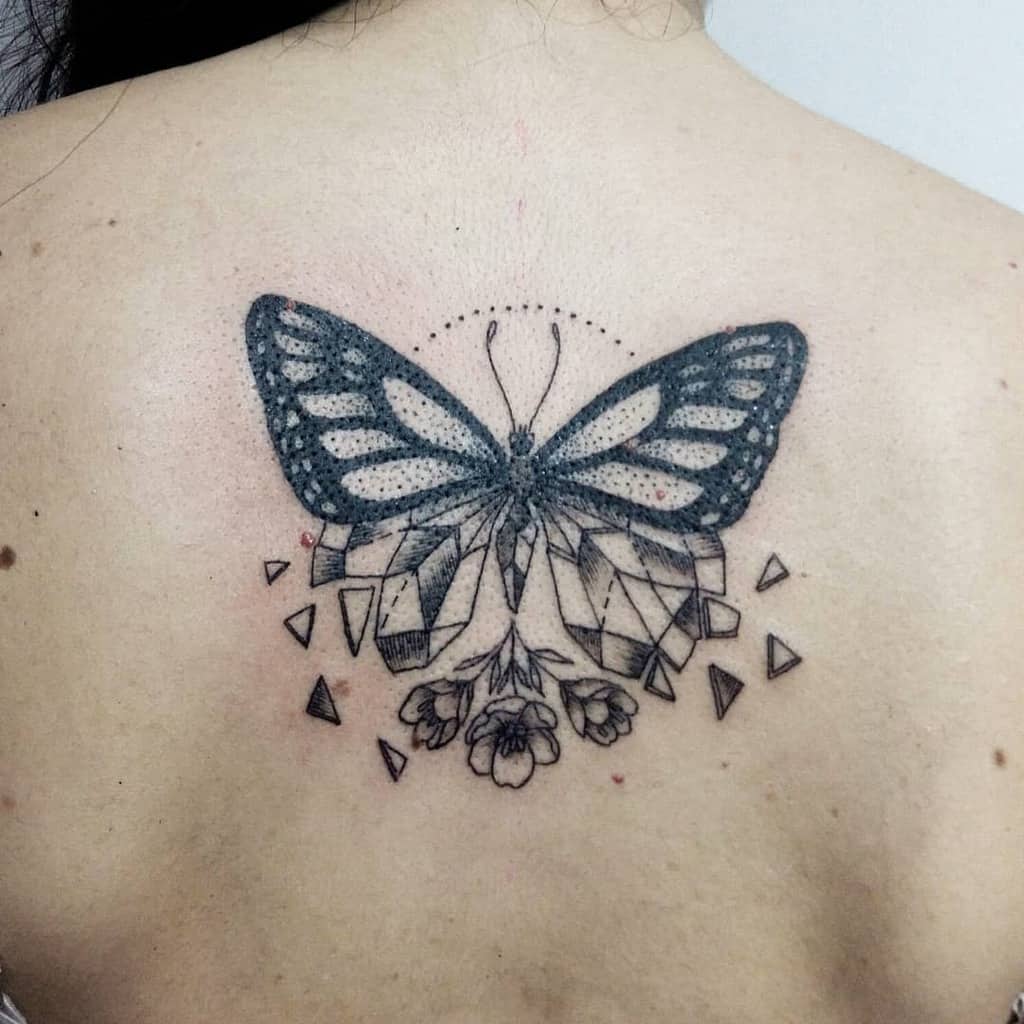 Geometric black butterfly tattoo with floral elements on a person's upper back