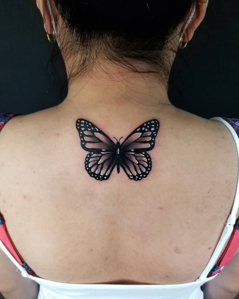 A black butterfly tattoo adorns a person's upper back, its delicate wings captured in striking black and white detail