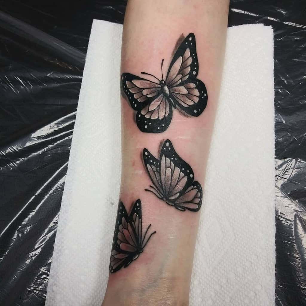 Three black butterflies and one grey butterfly tattooed on an arm with a white paper towel underneath