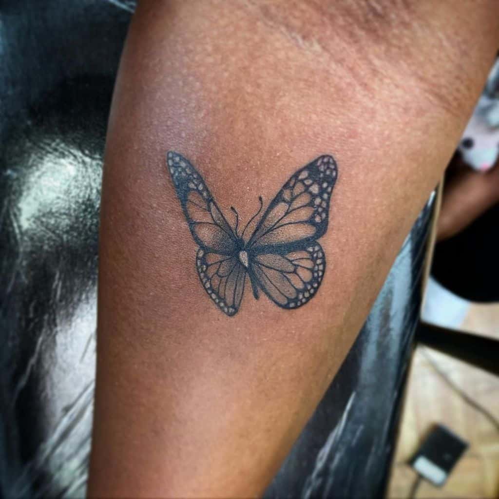 Stunning black butterfly tattoo on a person's arm, featuring intricate gray details