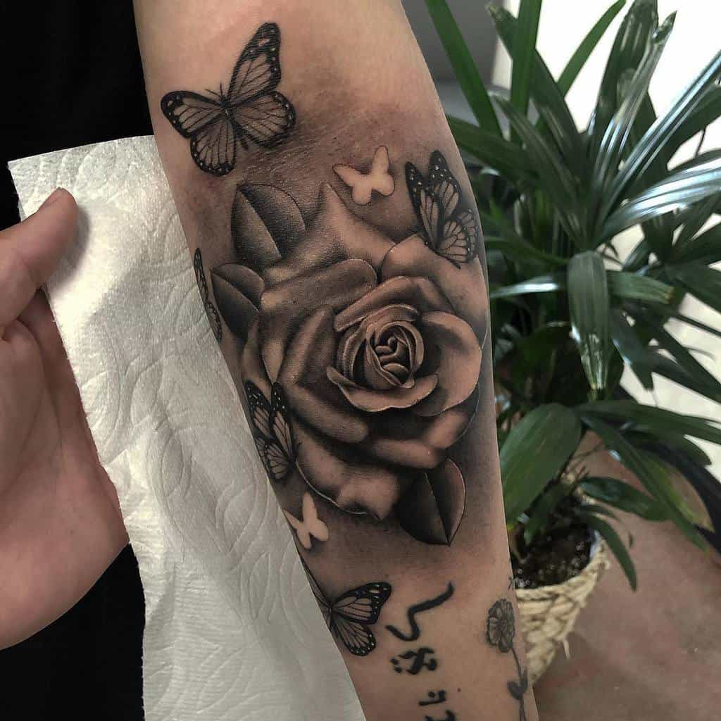 Forearm tattoo of a large rose surrounded by intricate black butterflies in black and white