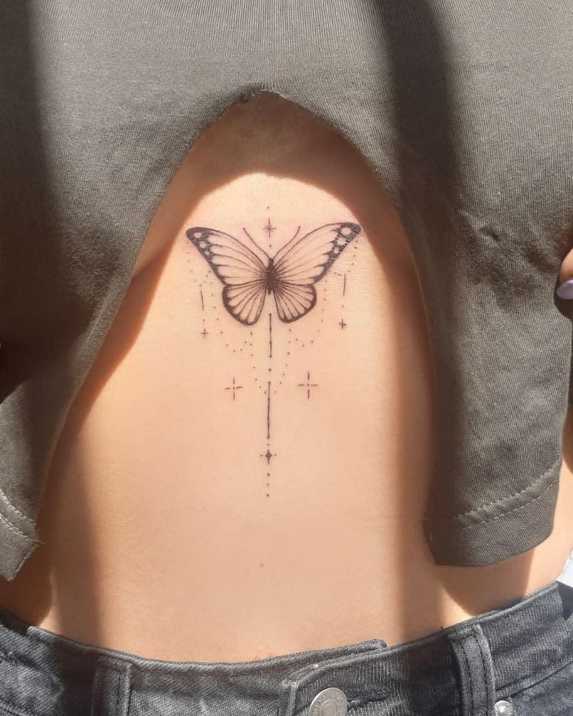 A detailed black butterfly tattoo with stars adorns a person's upper abdomen