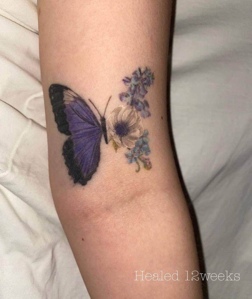 Realistic butterfly and floral tattoo on the arm, featuring a deep purple wing blending into delicate flowers for a soft, artistic look.
