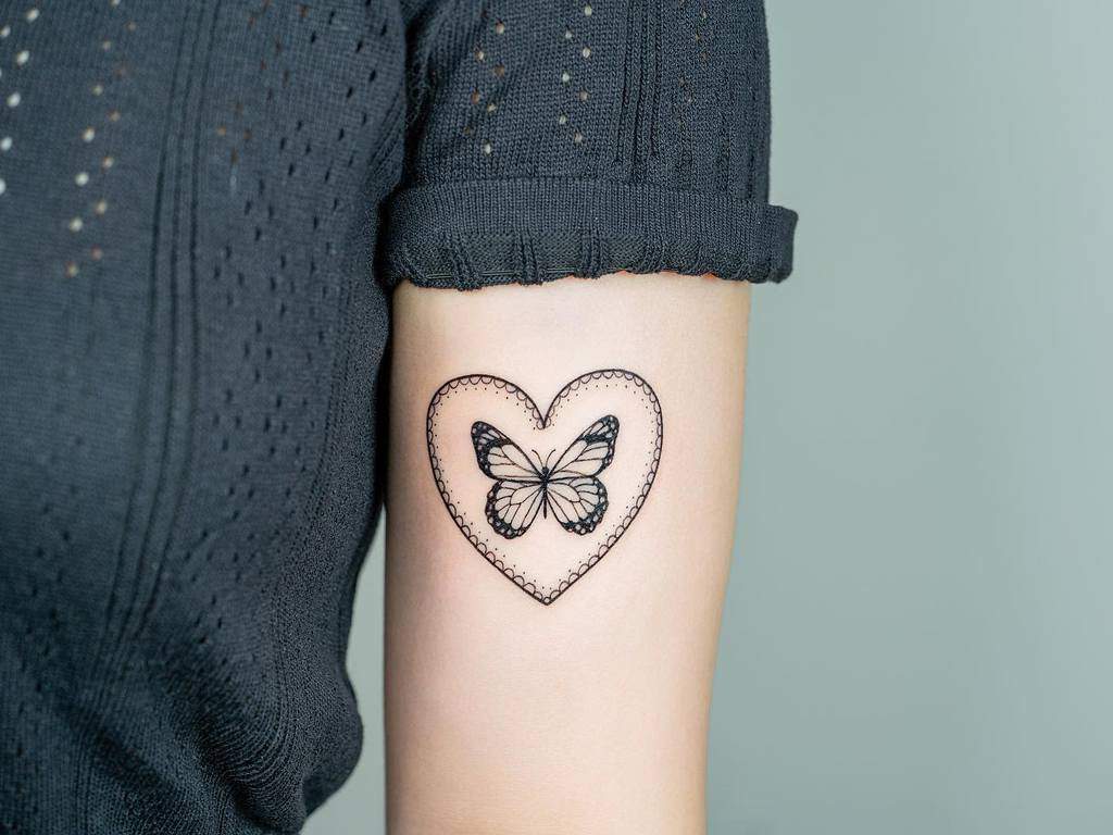 Tattoo of a black butterfly inside a heart outline on a person's upper arm