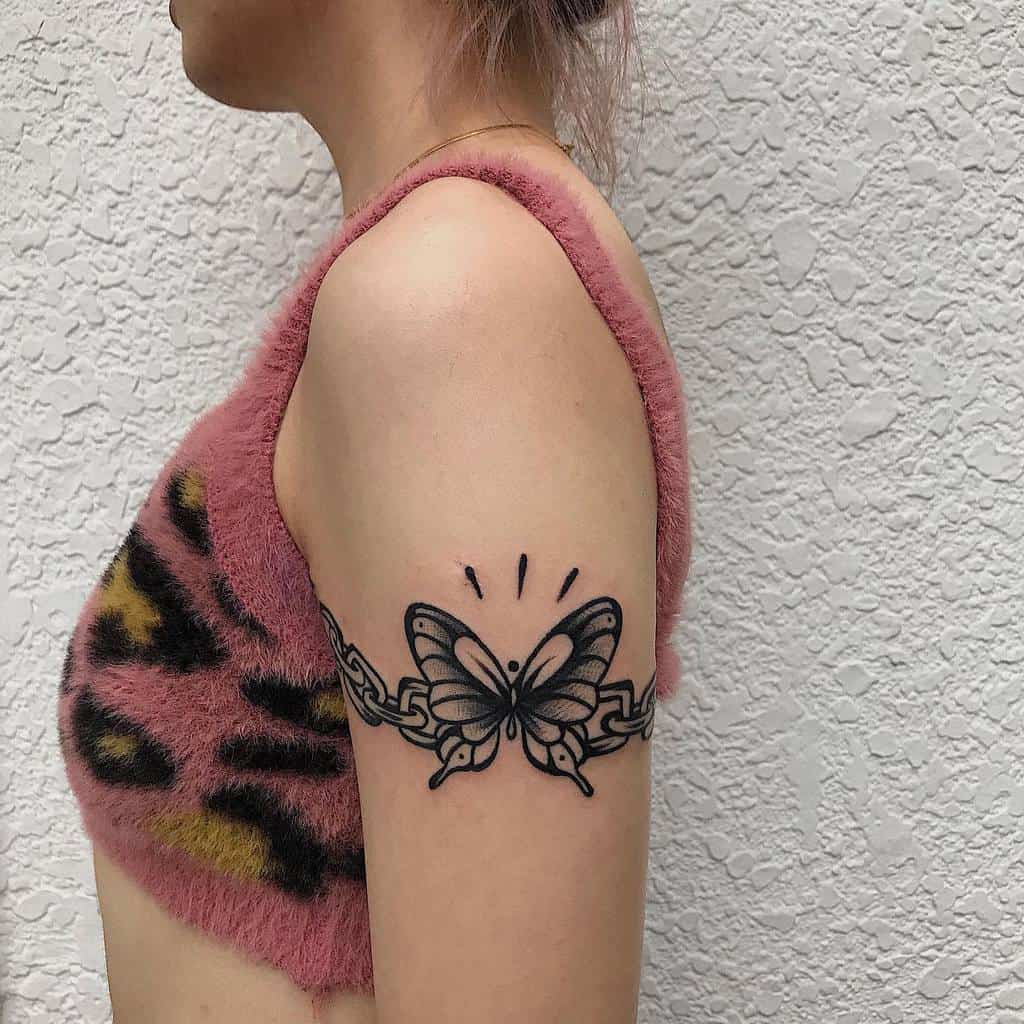 A woman with a black butterfly chain tattoo on the upper arm