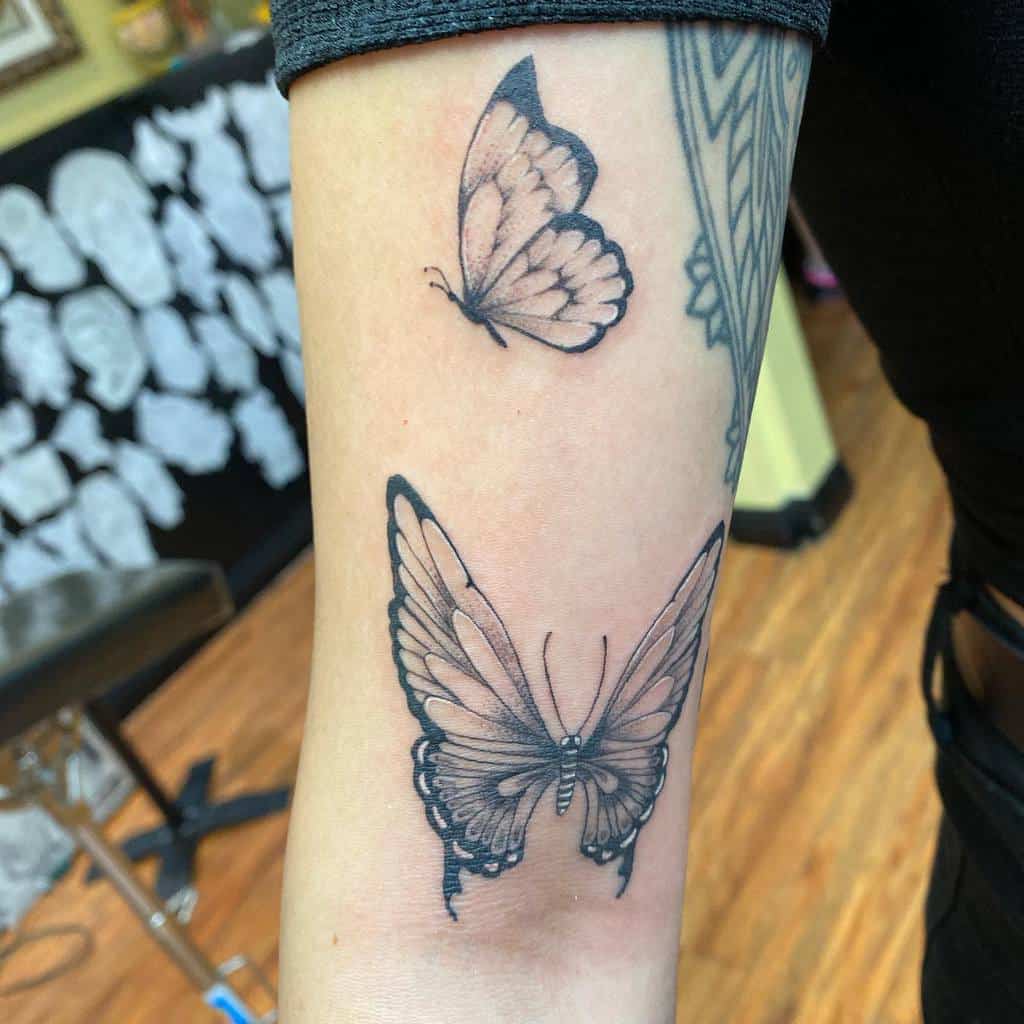 Two black butterfly tattoos adorn a person's arm, with one larger butterfly positioned gracefully below a smaller one